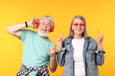 Photo of Senior couple in stylish outfits making rock gestures on orange background
