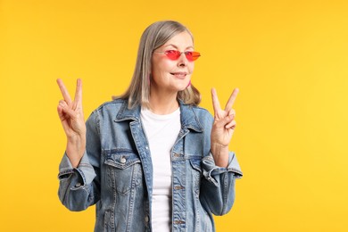 Photo of Senior woman in stylish outfit showing v-signs on orange background