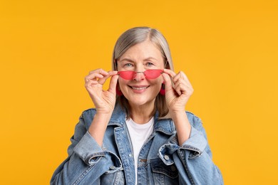 Photo of Senior woman wearing stylish sunglasses on orange background