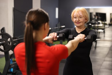 Photo of Senior woman exercising with dumbbells supervised by professional trainer in gym, selective focus
