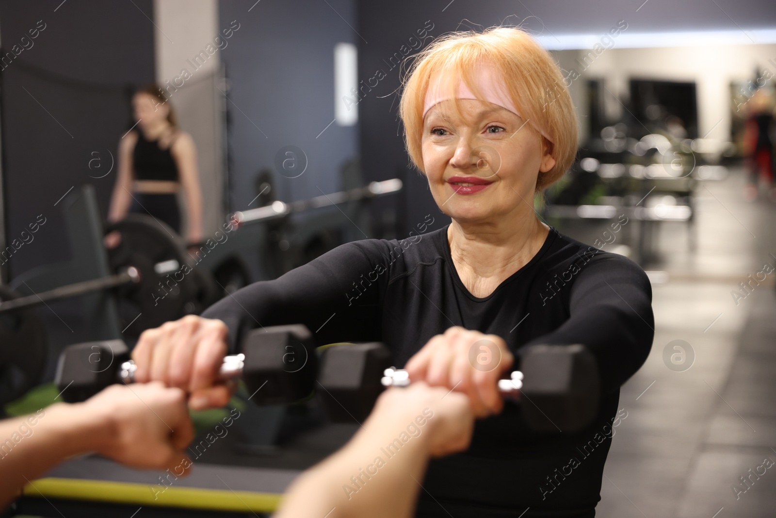 Senior woman exercising with dumbbells supervised by professional trainer in gym, closeup Photo of Senior woman exercising with dumbbells supervised by professional trainer in gym, closeup