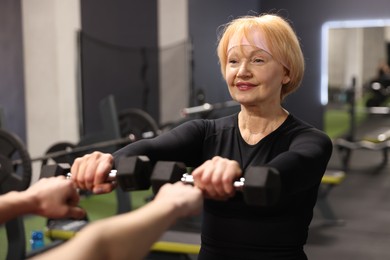 Photo of Senior woman exercising with dumbbells supervised by professional trainer in gym, closeup