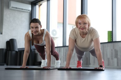 Photo of Senior woman and professional trainer exercising on yoga mat in gym, low angle view