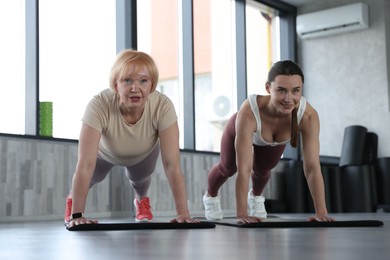 Photo of Senior woman and professional trainer exercising on yoga mat in gym, low angle view