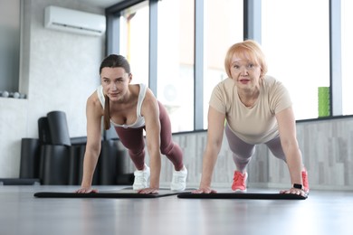 Photo of Senior woman and professional trainer exercising on yoga mat in gym, low angle view