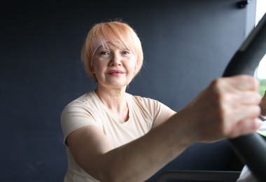 Photo of Senior woman training on elliptical machine in gym