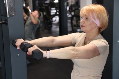 Photo of Senior woman training with dumbbells in gym