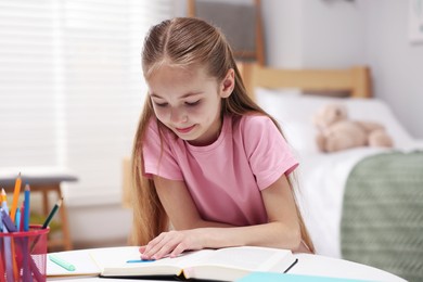 Photo of Dyslexia. Little girl reading book at table indoors