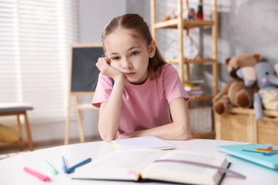 Photo of Dyslexia. Upset little girl reading book at table indoors