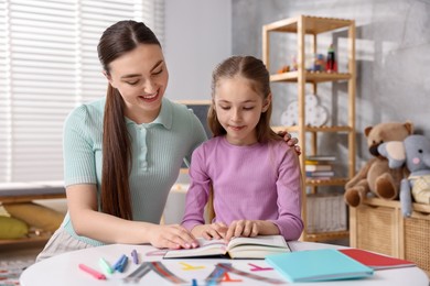 Photo of Dyslexia. Mother and her daughter reading book at table indoors