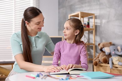 Photo of Dyslexia. Mother and her daughter reading book at table indoors