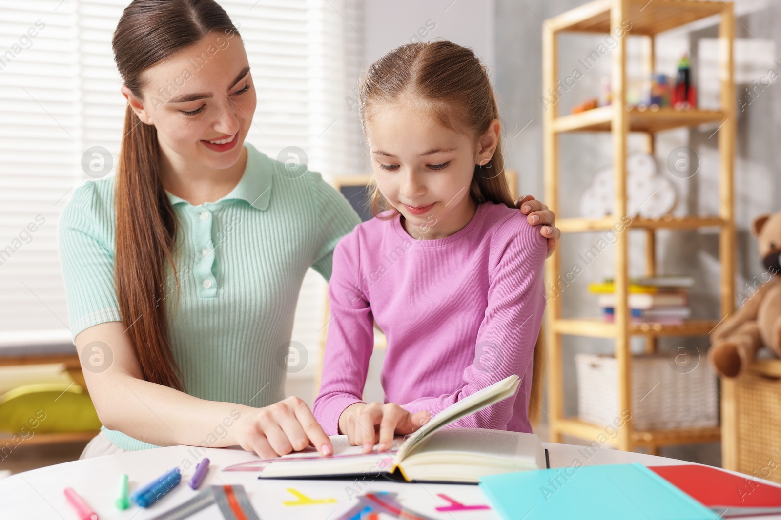 Dyslexia. Mother and her daughter reading book at table indoors Photo of Dyslexia. Mother and her daughter reading book at table indoors