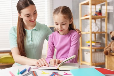 Photo of Dyslexia. Mother and her daughter reading book at table indoors