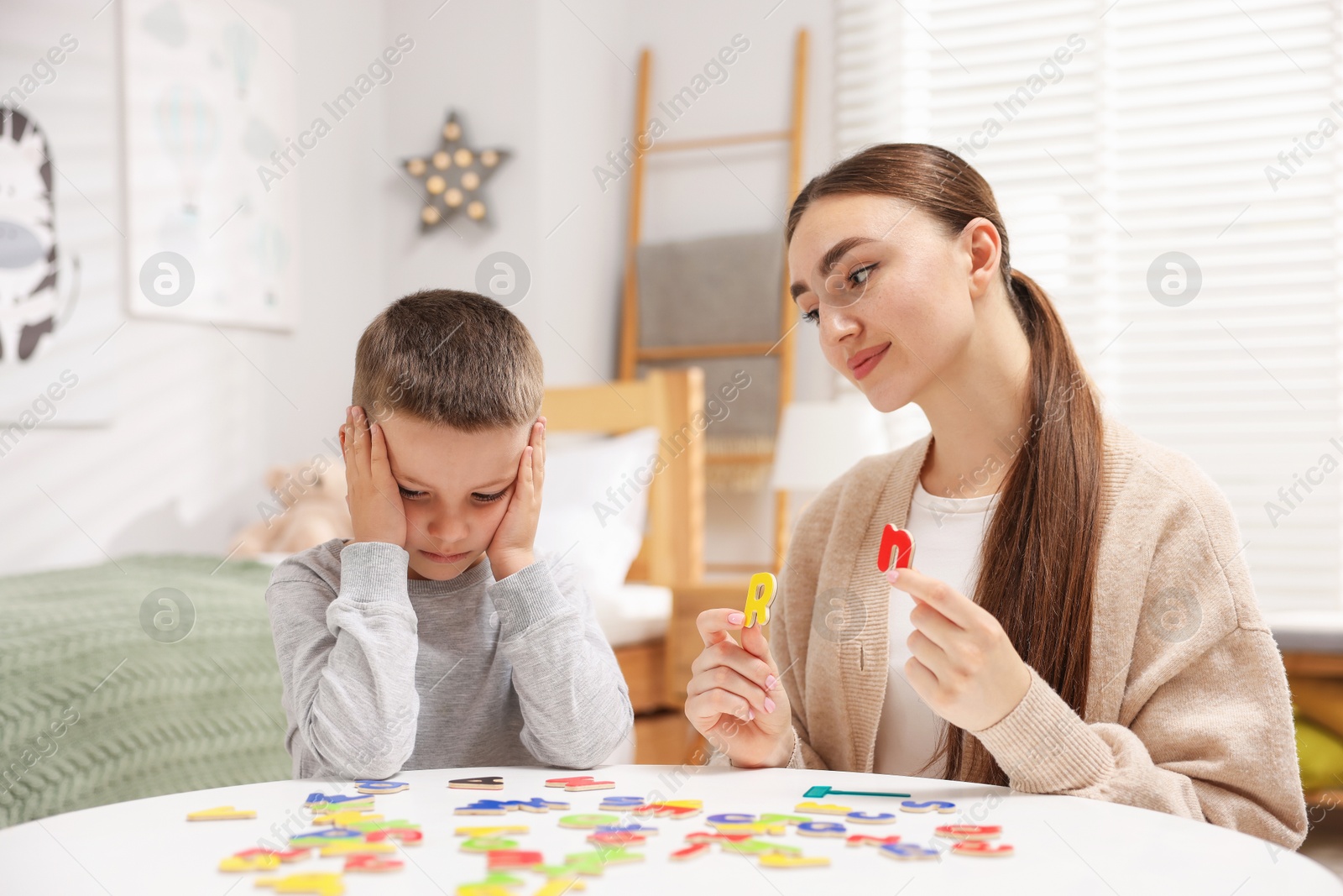 Dyslexia. Mother and her son learning letters at table indoors Photo of Dyslexia. Mother and her son learning letters at table indoors