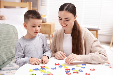 Photo of Dyslexia. Mother and her son learning letters at table indoors