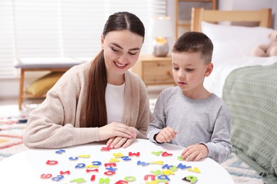 Photo of Dyslexia. Mother and her son learning letters at table indoors
