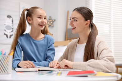 Photo of Dyslexia. Mother and her daughter reading book at table indoors