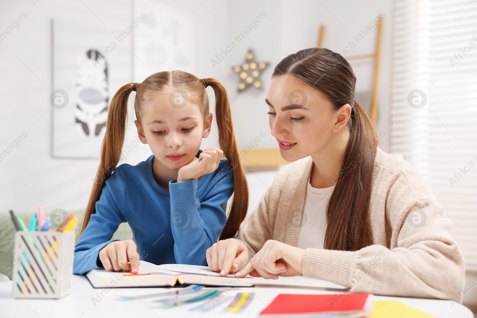 Dyslexia. Mother and her daughter reading book at table indoors Photo of Dyslexia. Mother and her daughter reading book at table indoors
