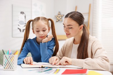 Photo of Dyslexia. Mother and her daughter reading book at table indoors
