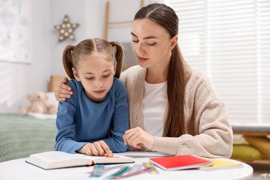 Photo of Dyslexia. Mother and her daughter reading book at table indoors