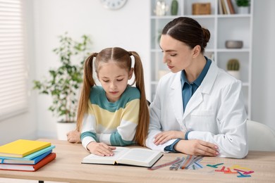 Photo of Dyslexia treatment. Pediatrician working with little girl at table indoors