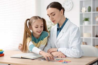 Photo of Dyslexia treatment. Pediatrician working with little girl at table indoors
