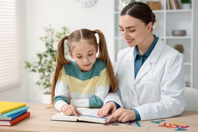 Photo of Dyslexia treatment. Pediatrician working with little girl at table indoors
