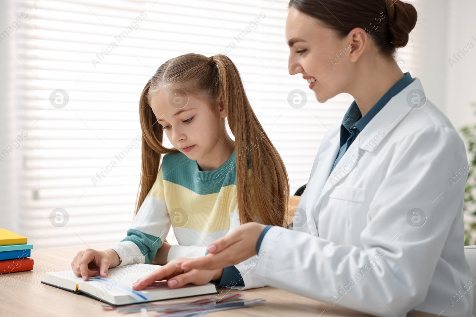 Dyslexia treatment. Pediatrician working with little girl at table indoors Photo of Dyslexia treatment. Pediatrician working with little girl at table indoors