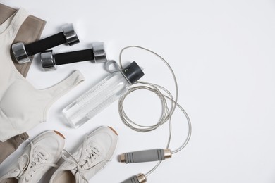 Photo of Sportswear, sneakers, dumbbells, skipping rope and water bottle on white background, flat lay. Space for text
