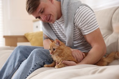 Photo of Man with cute ginger cat on sofa at home, selective focus