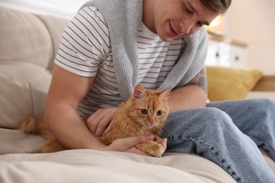 Photo of Man with cute ginger cat on sofa at home, selective focus