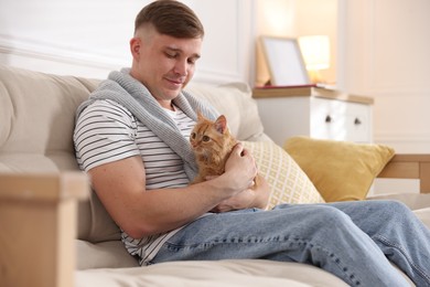 Photo of Man with cute ginger cat on sofa at home