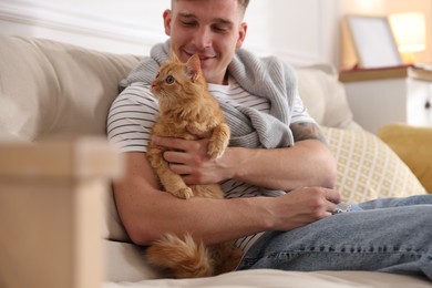 Photo of Man with cute ginger cat on sofa at home