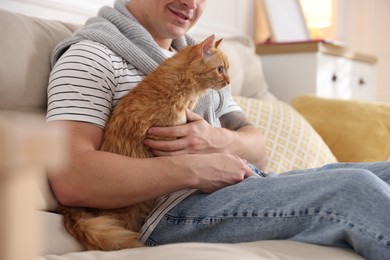 Photo of Man with cute ginger cat on sofa at home, closeup