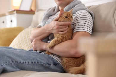 Photo of Man with cute ginger cat on sofa at home, closeup