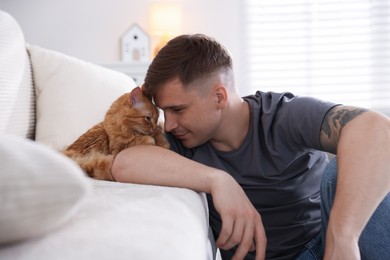 Photo of Man with cute ginger cat on sofa at home
