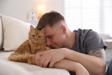 Photo of Man with cute ginger cat on sofa at home