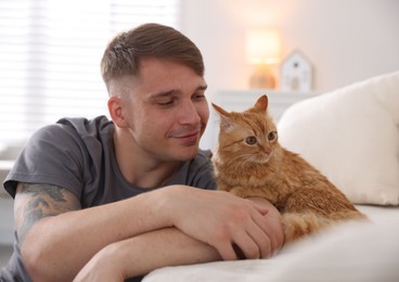 Photo of Man with cute ginger cat on sofa at home