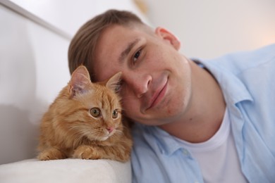 Photo of Man with cute ginger cat at home, selective focus