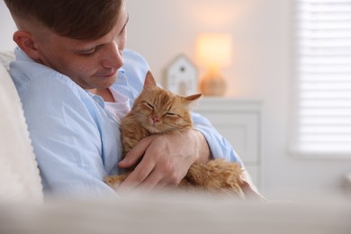 Photo of Man with cute ginger cat on sofa at home