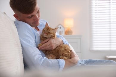 Photo of Man with cute ginger cat on sofa at home