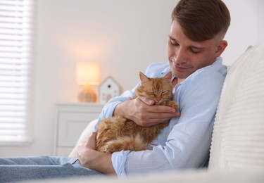 Photo of Man with cute ginger cat on sofa at home