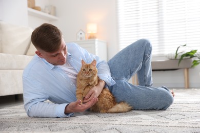 Photo of Man with cute ginger cat on rug at home