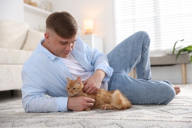 Photo of Man with cute ginger cat on rug at home