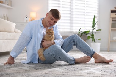 Photo of Man with cute ginger cat on rug at home