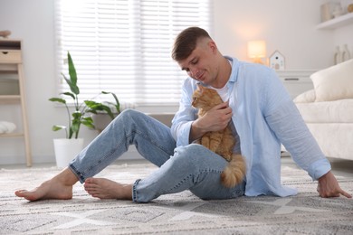 Photo of Man with cute ginger cat on rug at home