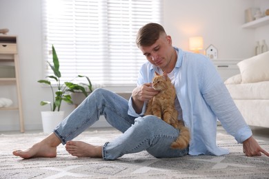 Photo of Man with cute ginger cat on rug at home