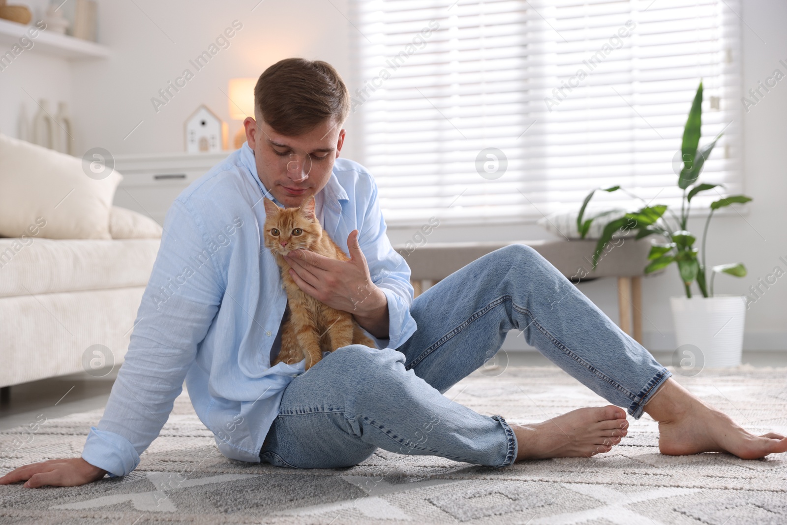 Man with cute ginger cat on rug at home Photo of Man with cute ginger cat on rug at home