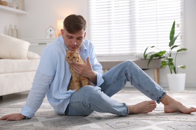 Photo of Man with cute ginger cat on rug at home