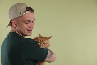 Photo of Man with cute ginger cat on light green background, space for text